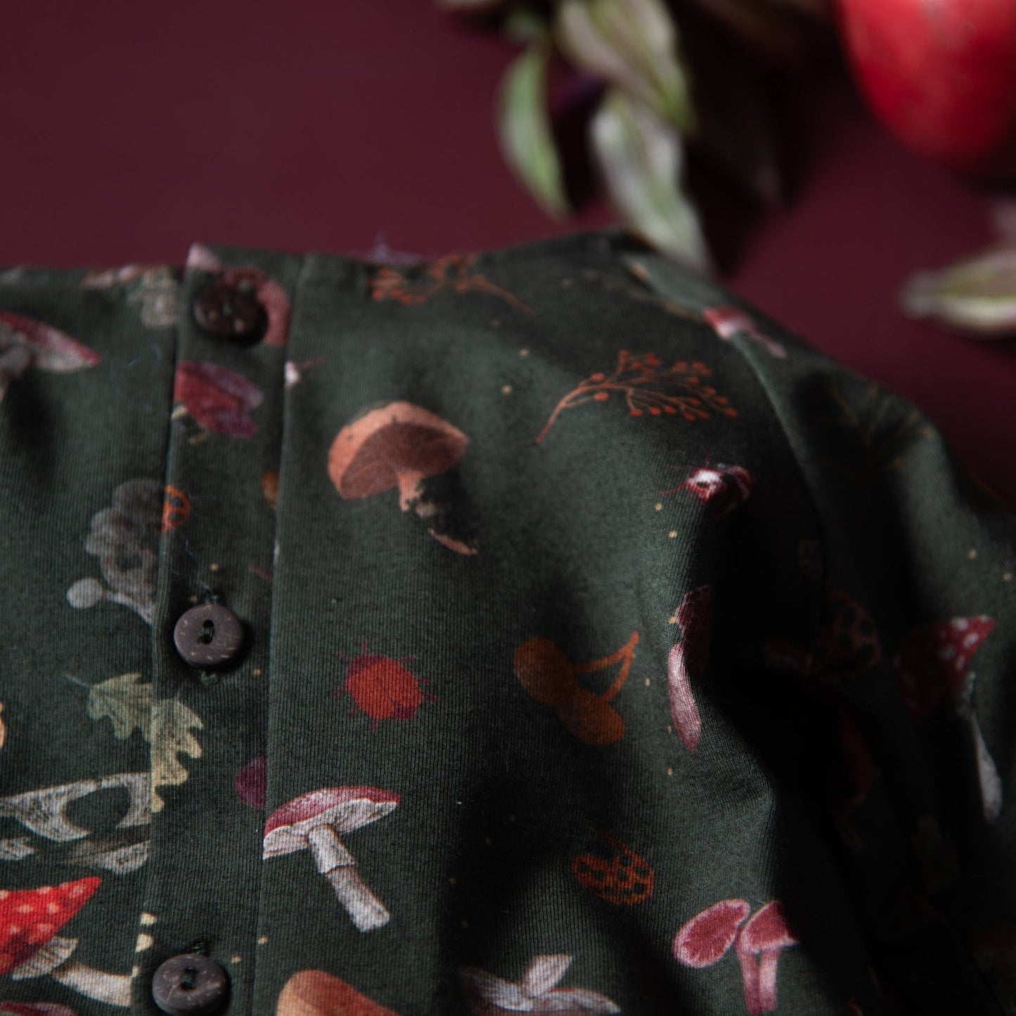 A close-up of the top of the green romper with buttons and mushroom patterns in warm earthy tones.