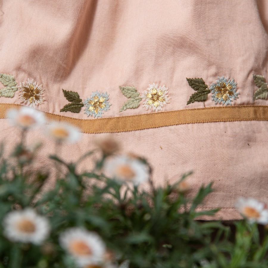 Close-up of Birdie Bliss dress showcasing embroidered bird and floral motifs, with greenery and flowers in the foreground.