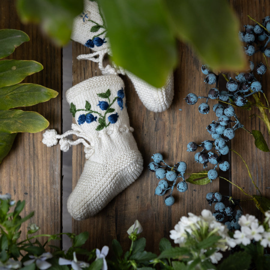 knitted and hand embroidered blueberries footies displayed on a wooden surface surrounded with greenery
