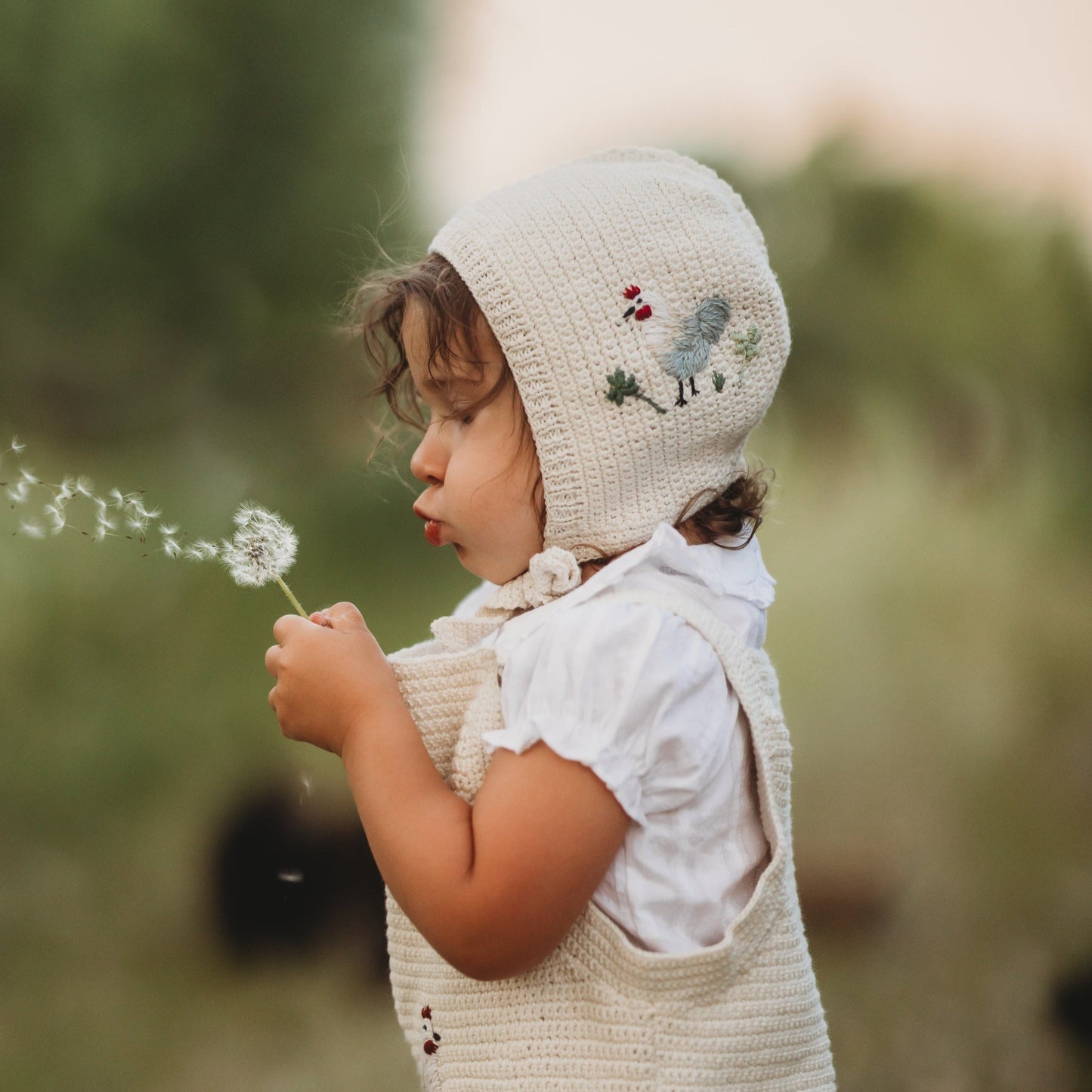 Baby wearing Chicken Bonnet - Marshmellow, holding a flower.