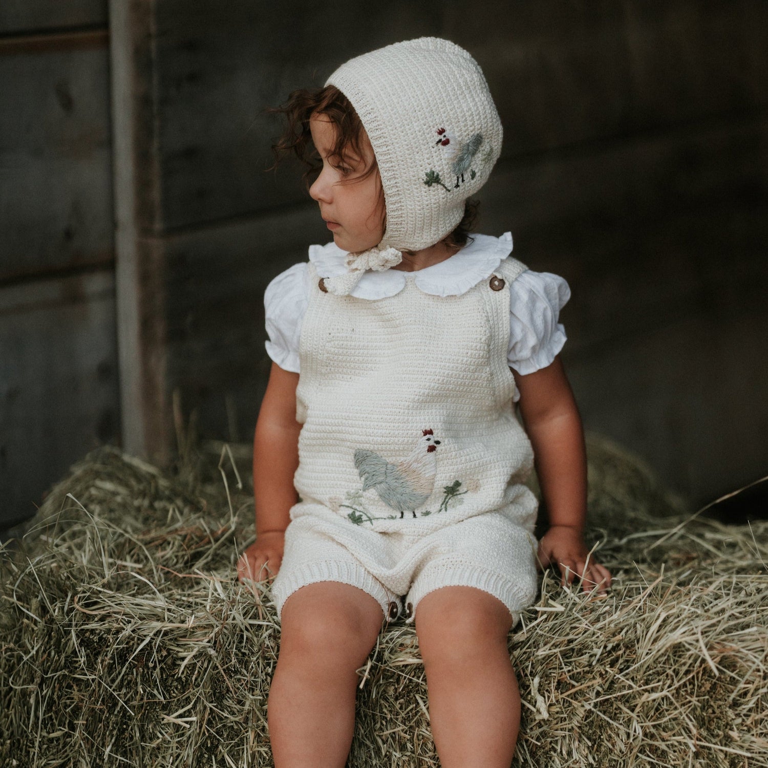Little Farm Romper - Malt, worn by a child with soft grass and shadows in the background.







