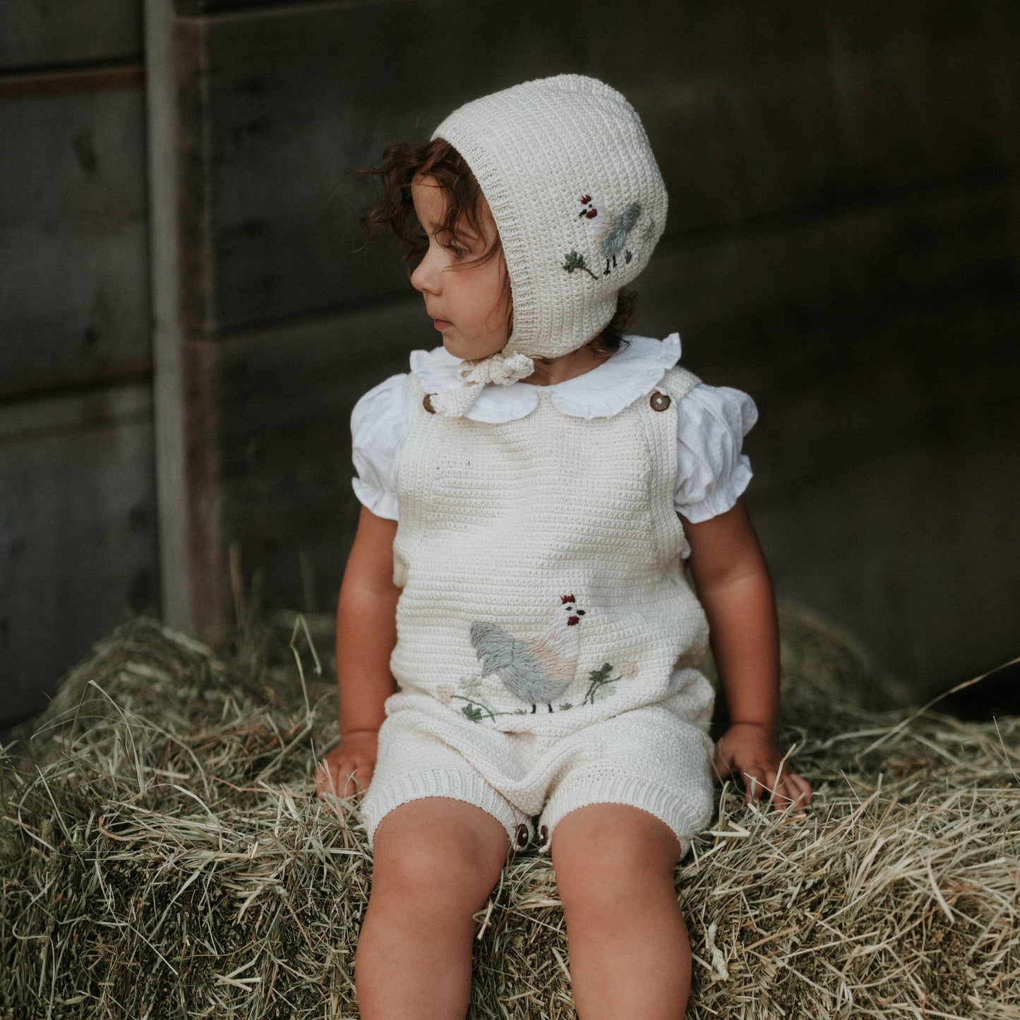 Child wearing Chicken Bonnet - Marshmellow with hay or grass around.