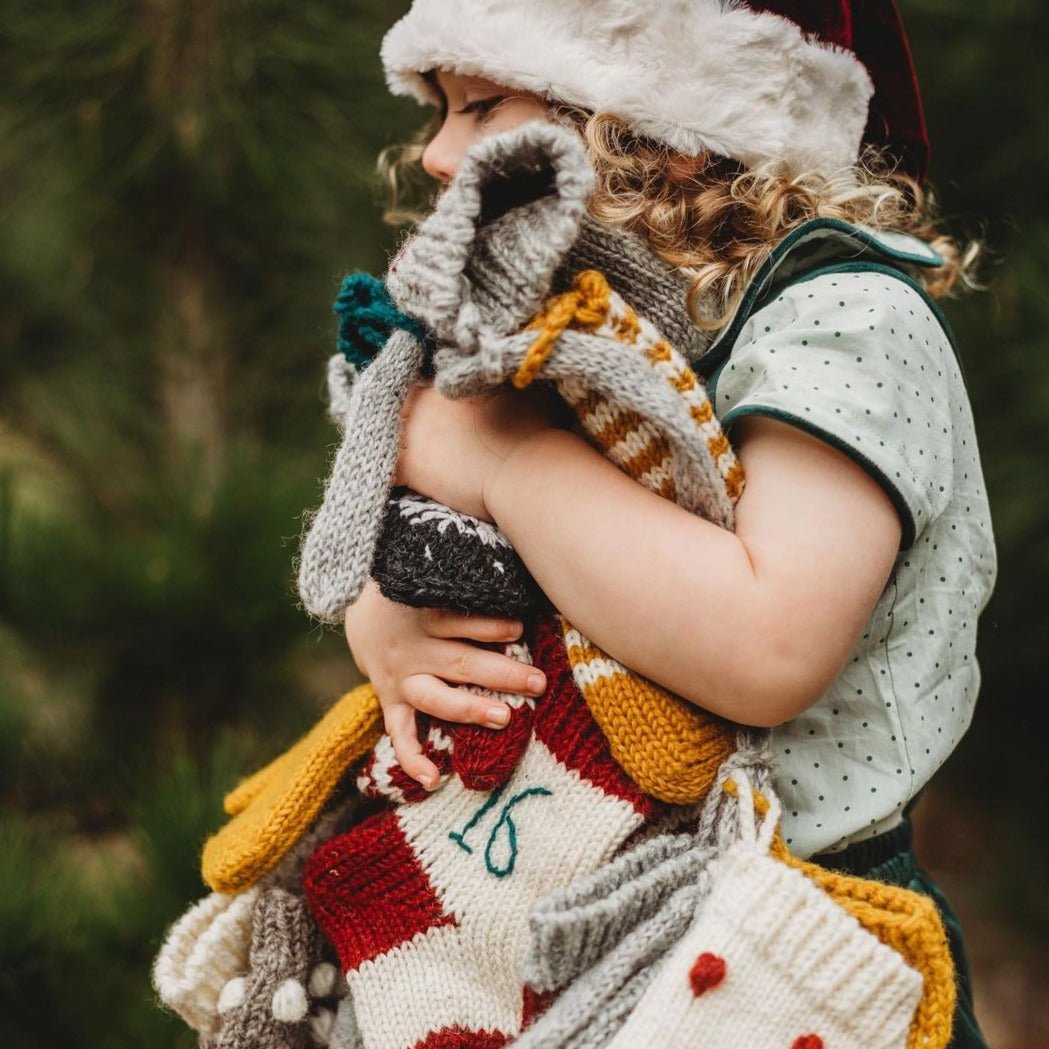 A collection of handcrafted Christmas stockings, hats, and mittens being held.