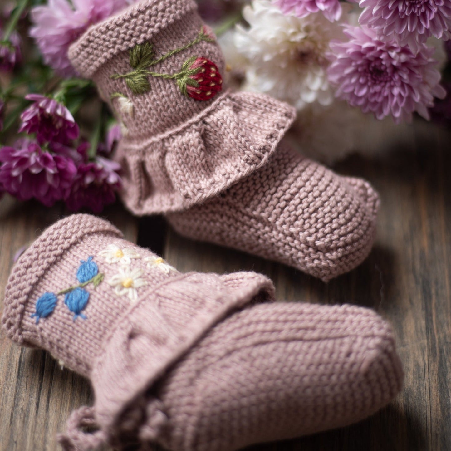Knitted booties with strawberry and blue floral embroidery displayed on wood.