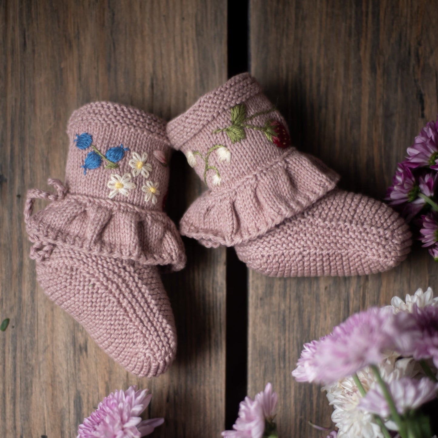 Pair of pink floral embroidered booties on a wooden surface with flowers.