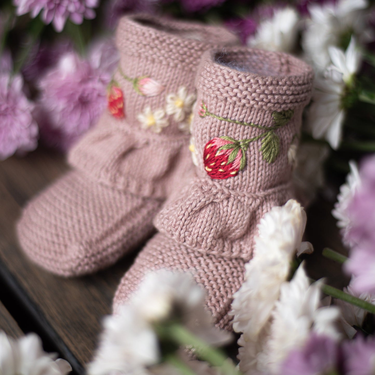 Close-up of strawberry and daisy embroidered pink booties among flowers.