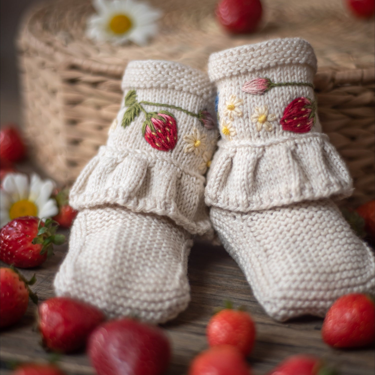 Close-up of knitted baby booties with hand-embroidered strawberries and flowers, highlighting their exquisite craftsmanship.
