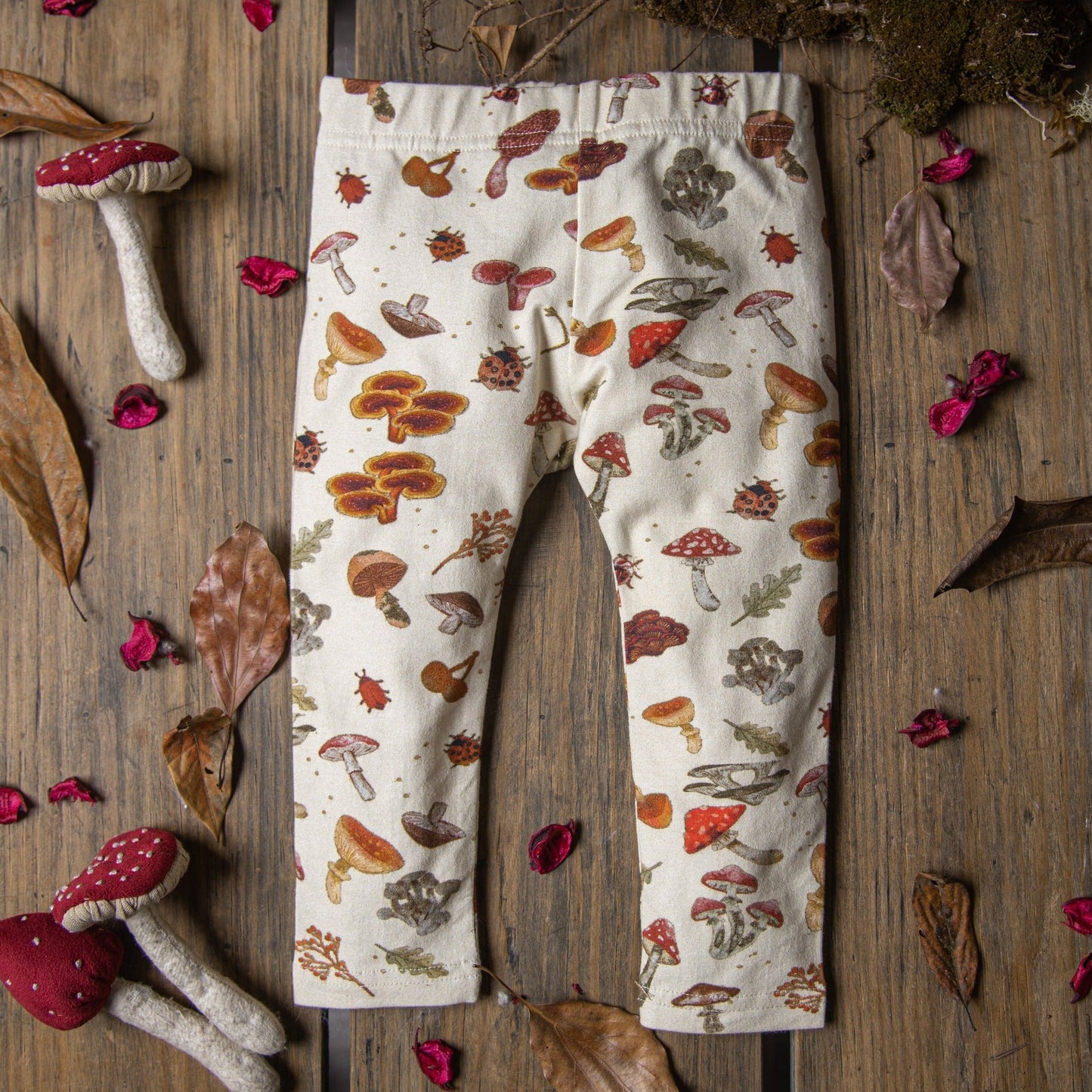 Flat lay of cream-colored baby leggings decorated with whimsical mushroom illustrations.
