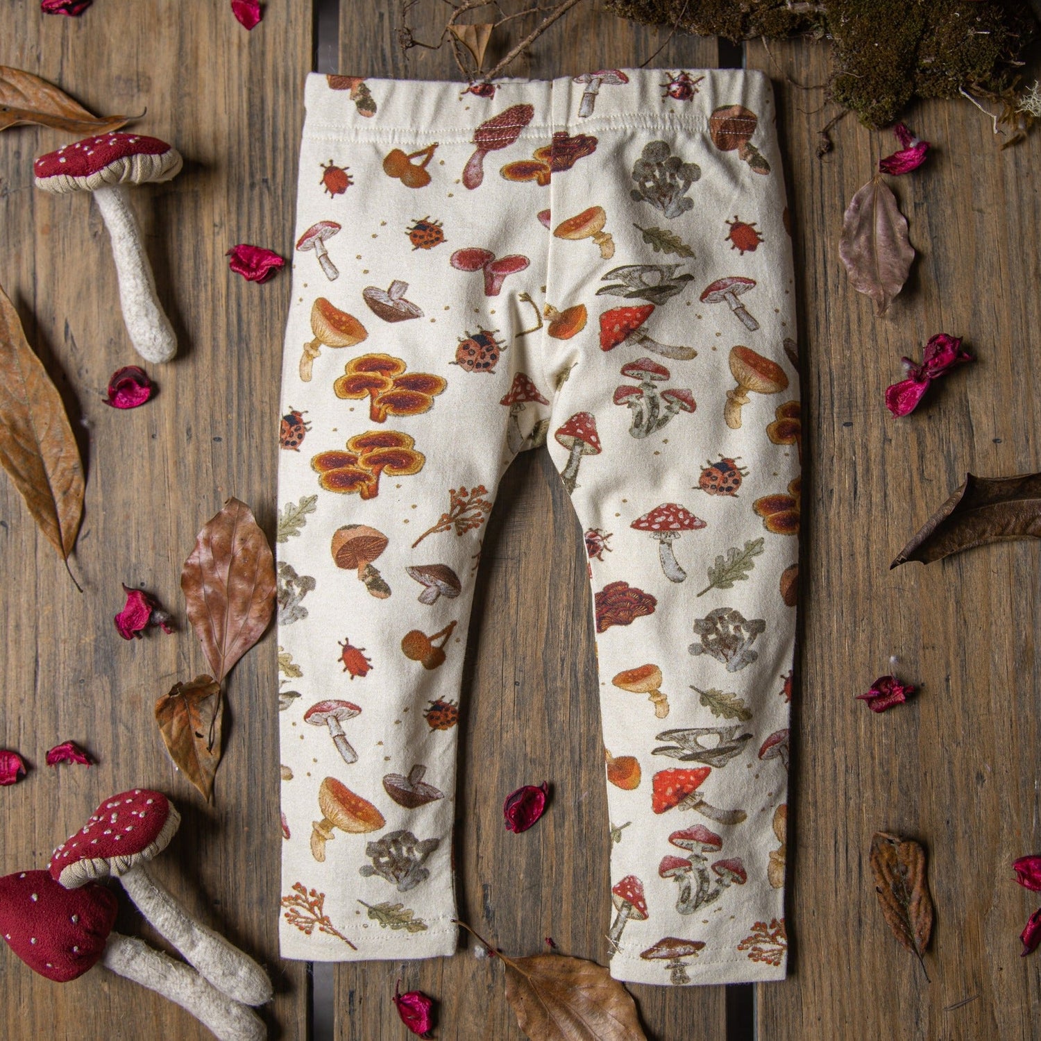 Flat lay of cream-colored baby leggings decorated with whimsical mushroom illustrations.
