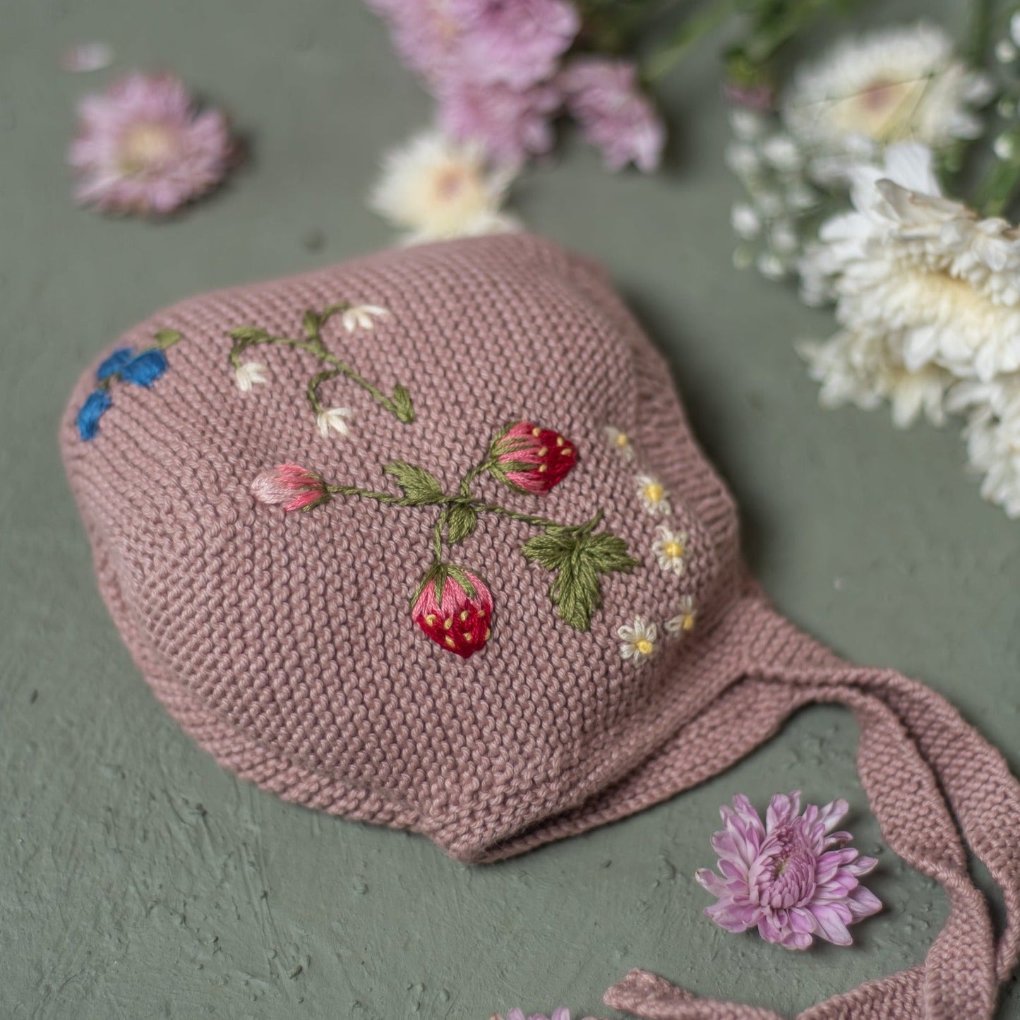 Child wearing pink embroidered bonnet holding an adult's hand

