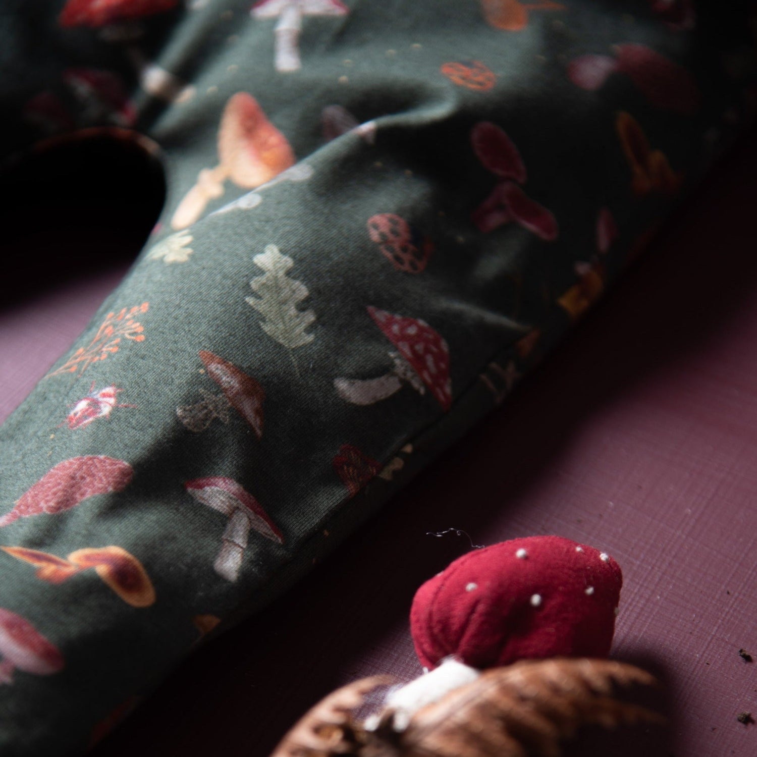A close-up of the leg of the green romper showing the detailed mushroom and leaf print.