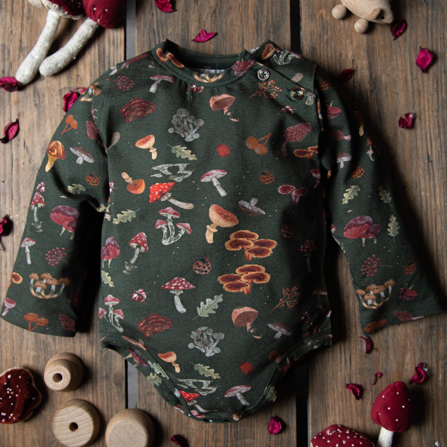 A dark green mushroom-print bodysuit displayed on a wooden surface with toys.