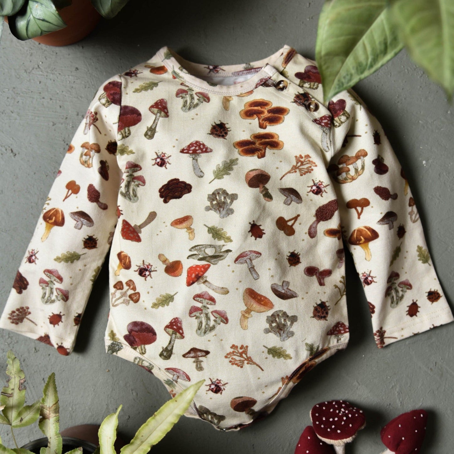 A mushroom-print bodysuit laid out with toy mushrooms beside it.