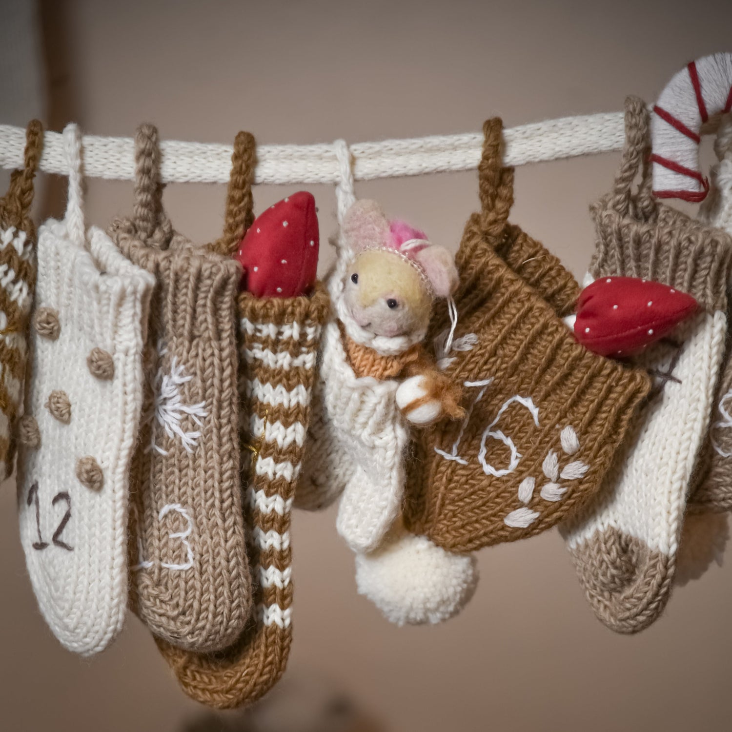 Close-up of a section of the cream wool Advent Calendar, highlighting the details of the handcrafted mittens, hats, and socks with visible numbers.