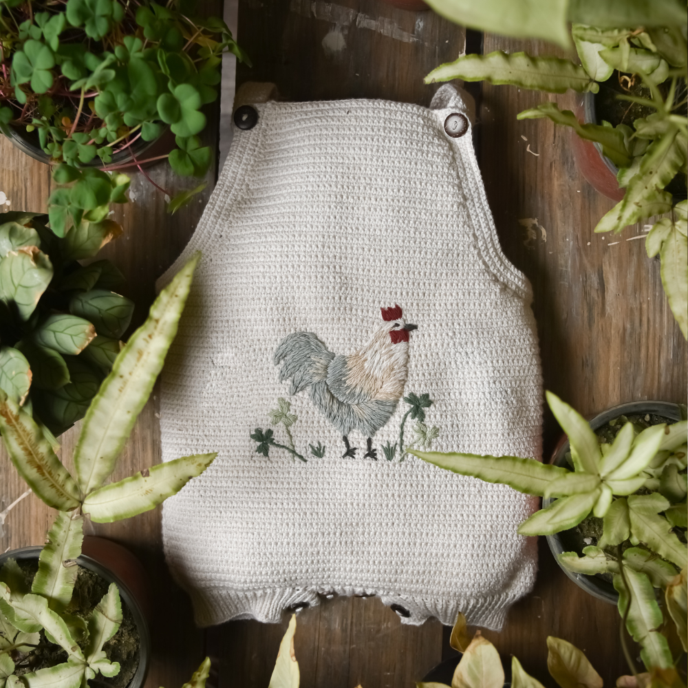 Little Farm Romper - Malt, with floral accents and greenery in the background.