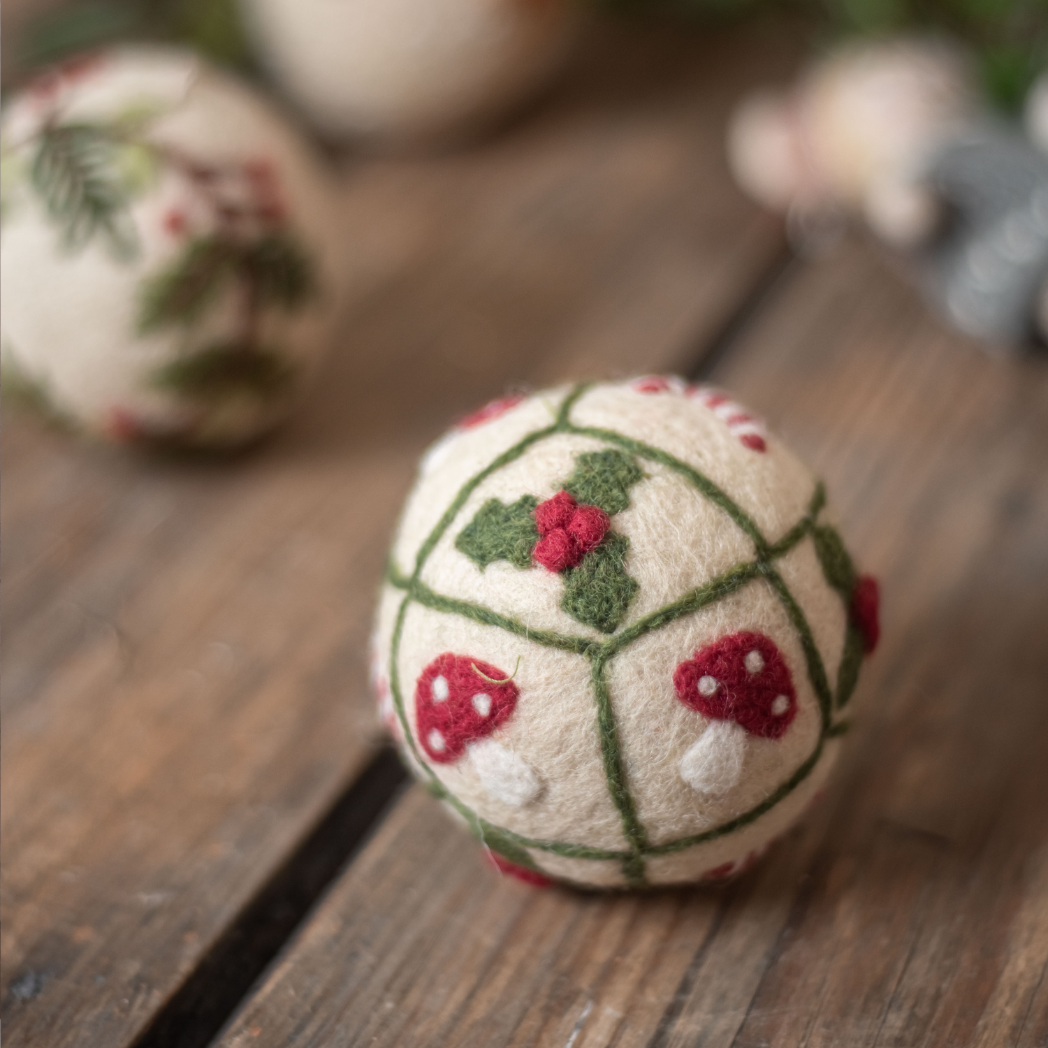 Bauble Grid Ornament with embroidered mushrooms and holiday motifs, placed on a table with dimly lit Christmas decorations in the background.