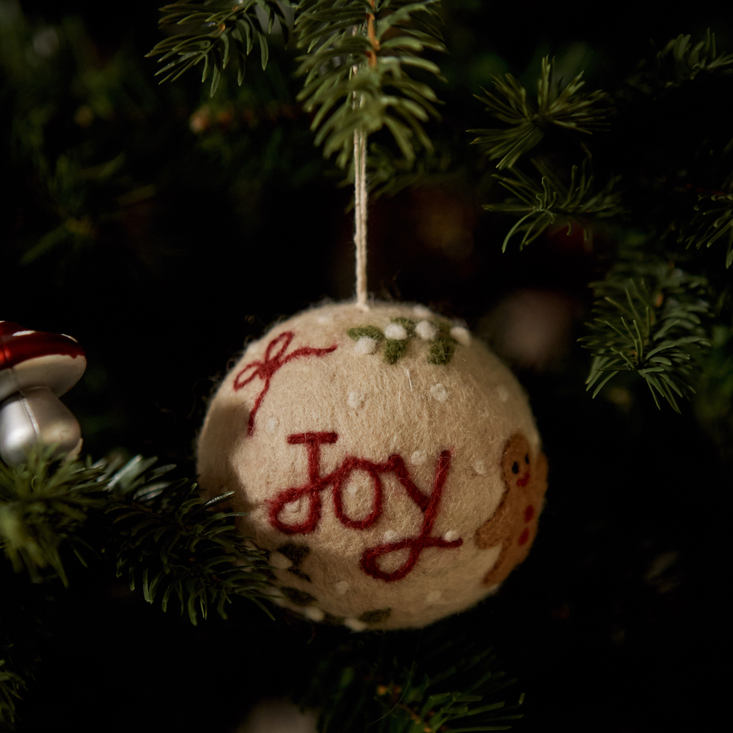 Bauble Joy Ornament displayed on a Christmas tree, highlighting its festive embroidery and charming design amid other decorations.