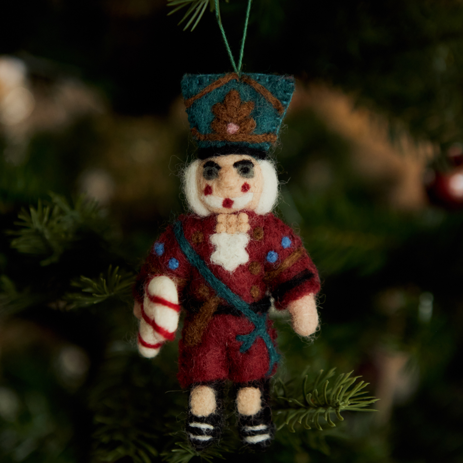 Nutcracker ornament in red with intricate embroidery hanging on a Christmas tree