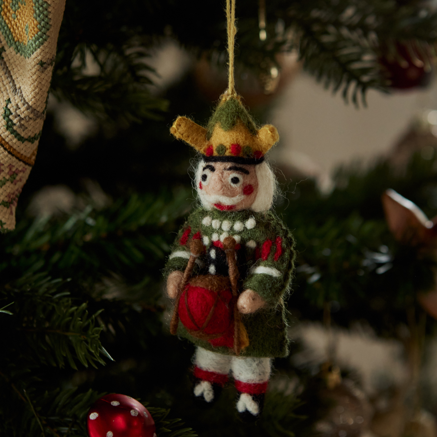 Nutcracker ornament in green with intricate embroidery hanging on a Christmas tree