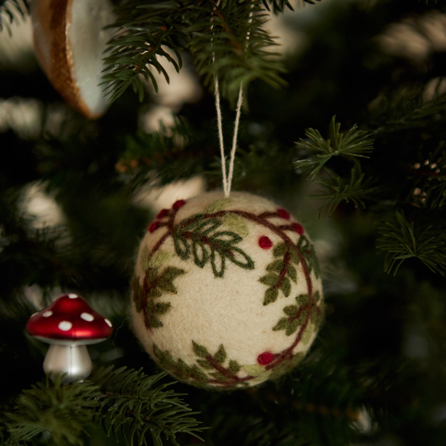 Bauble ornament with embroidered wreath design hanging on a Christmas tree