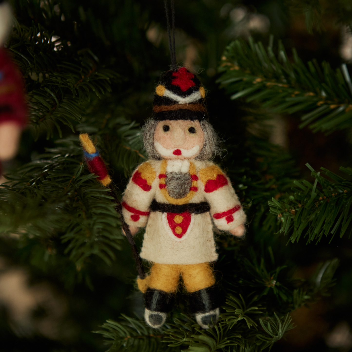 Nutcracker ornament in cream with intricate embroidery hanging on a Christmas tree