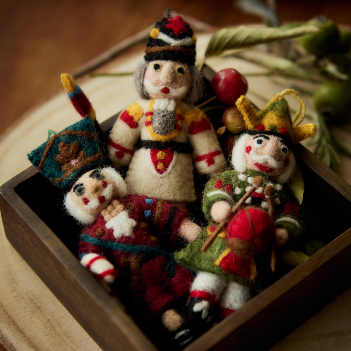 Various Nutcracker ornaments in cream, green, and red displayed in a wooden box