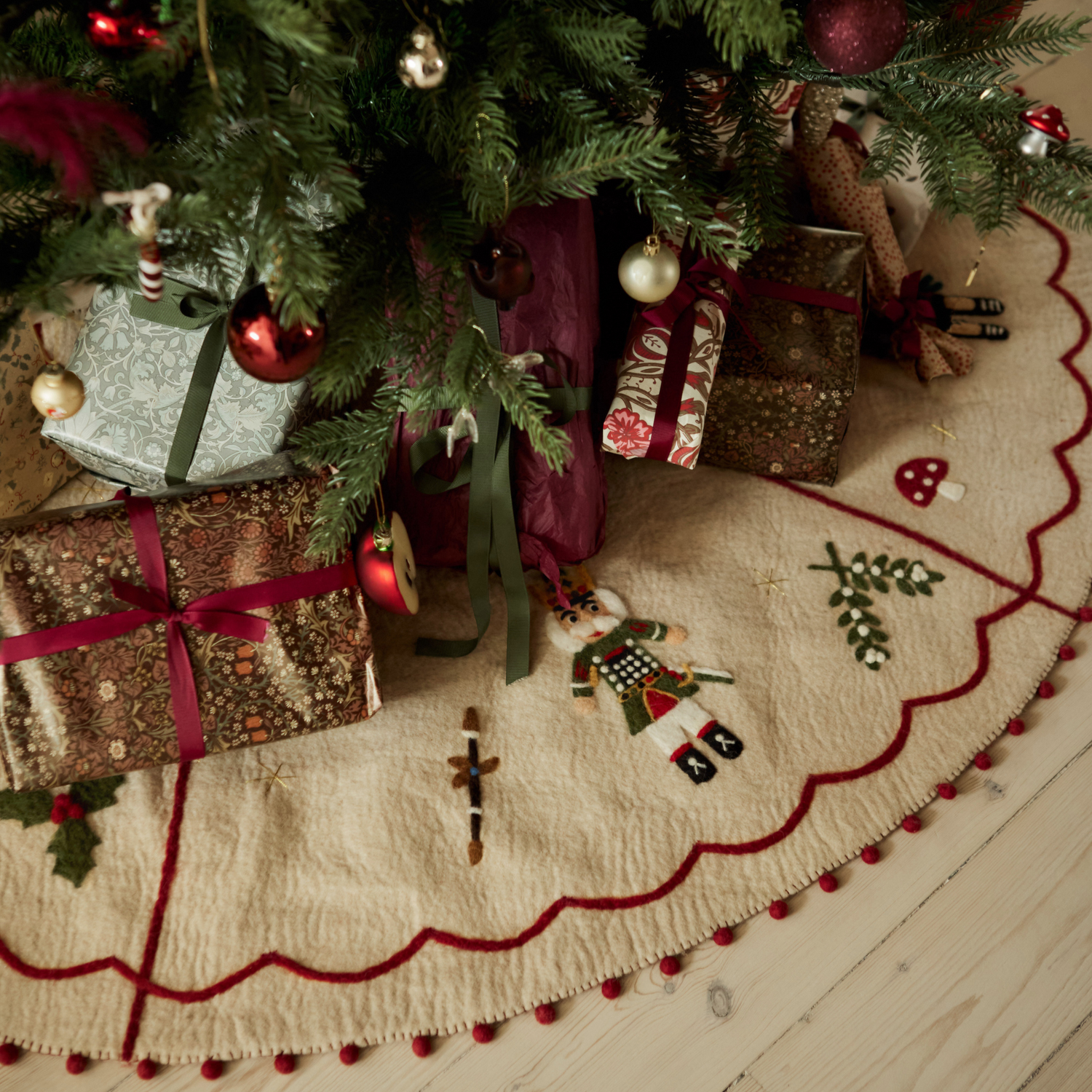 Christmas gifts arranged on the Nutcracker Heirloom Tree Rug beneath a decorated tree, showcasing intricate holiday details.