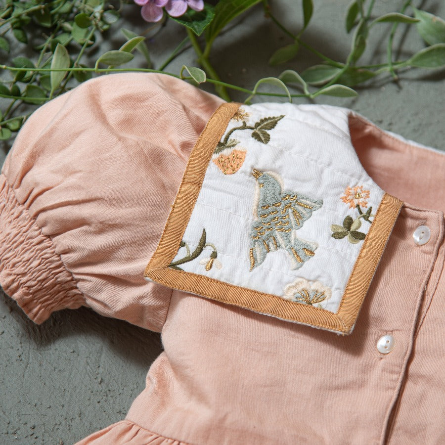 Close-up of the Birdie Bliss dress showing embroidered bird and floral motifs, with greenery in the background.







