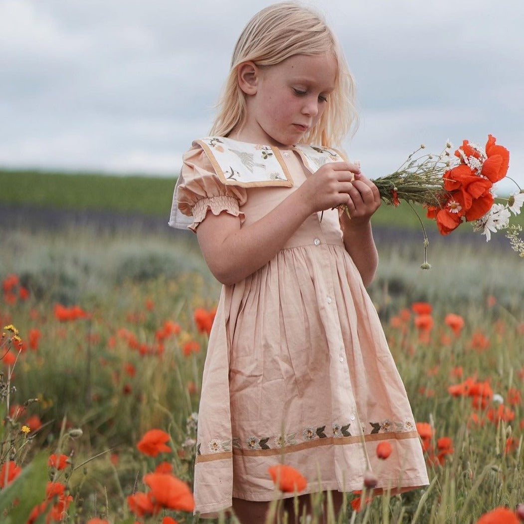 Girl wearing the Birdie Bliss dress in a flower field, holding flowers in her hands.







