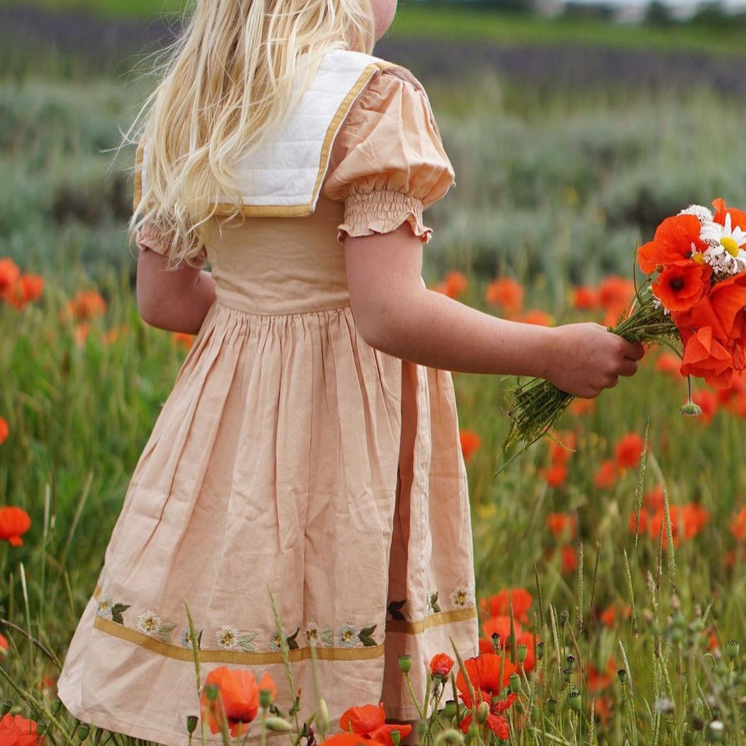 Child wearing Birdie Bliss dress in a field of flowers, holding flowers in hand.







