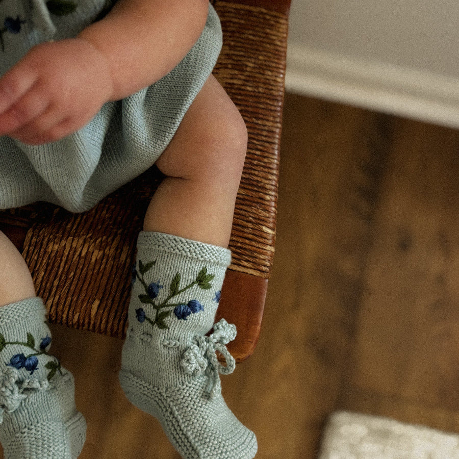 Close-up of a baby wearing the embroidered footies while seated on a wooden chair.
