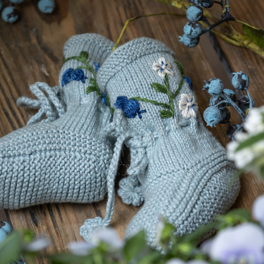 Flat lay of the embroidered footies surrounded by small blueberry sprigs.
