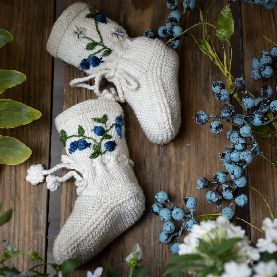 knitted and hand embroidered blueberries footies displayed on a wooden surface surrounded with greenery  