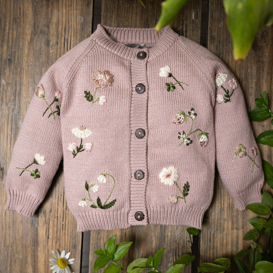 Flat lay of pastel flowers beside the cardigan showing nature-inspired details.