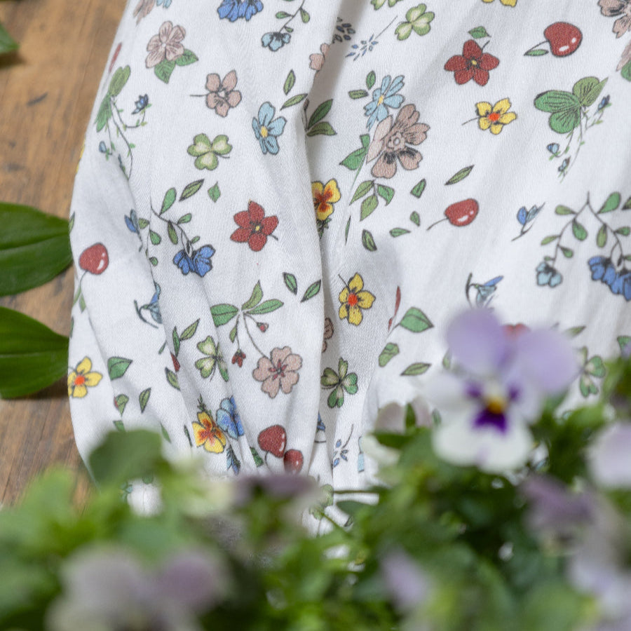 Close-up of white baby romper with colorful floral and cherry print on a wooden background
