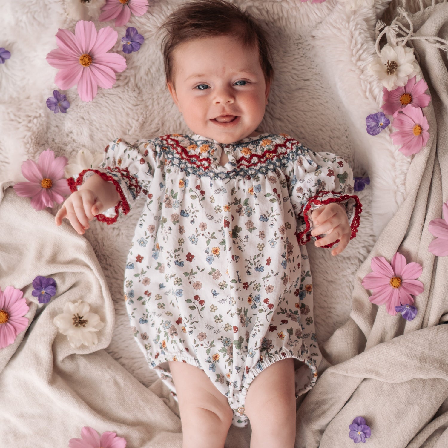 Baby in a floral romper surrounded by flowers on a soft fabric background
