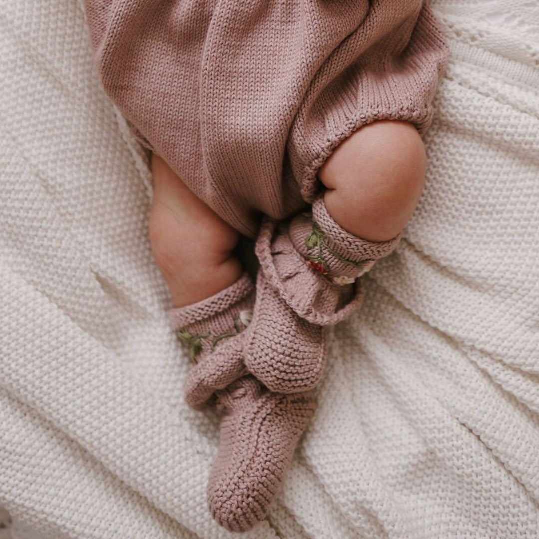 Baby wearing soft pink embroidered booties while resting on a blanket.