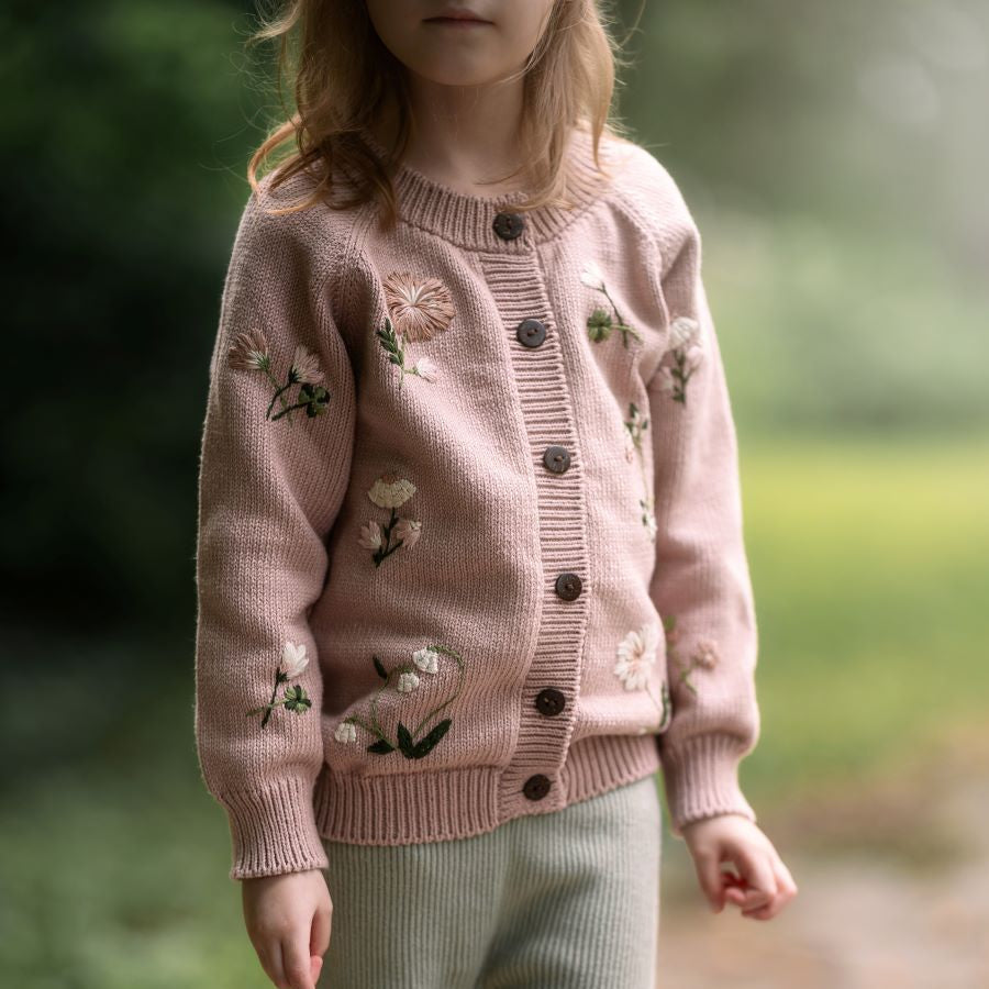 Child wearing a pink sweater with floral patterns outdoors on a path.
