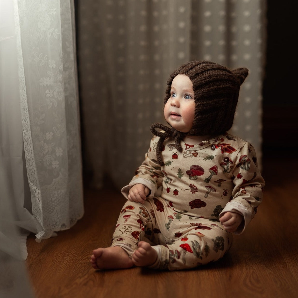 A baby wearing the mushroom-print bodysuit with a knit bonnet.