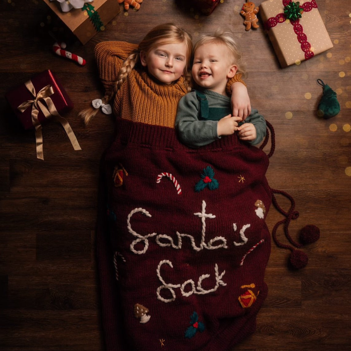 Red wool Santa sack with "Santa's Sack" embroidered, surrounded by festive decorations and ornaments.