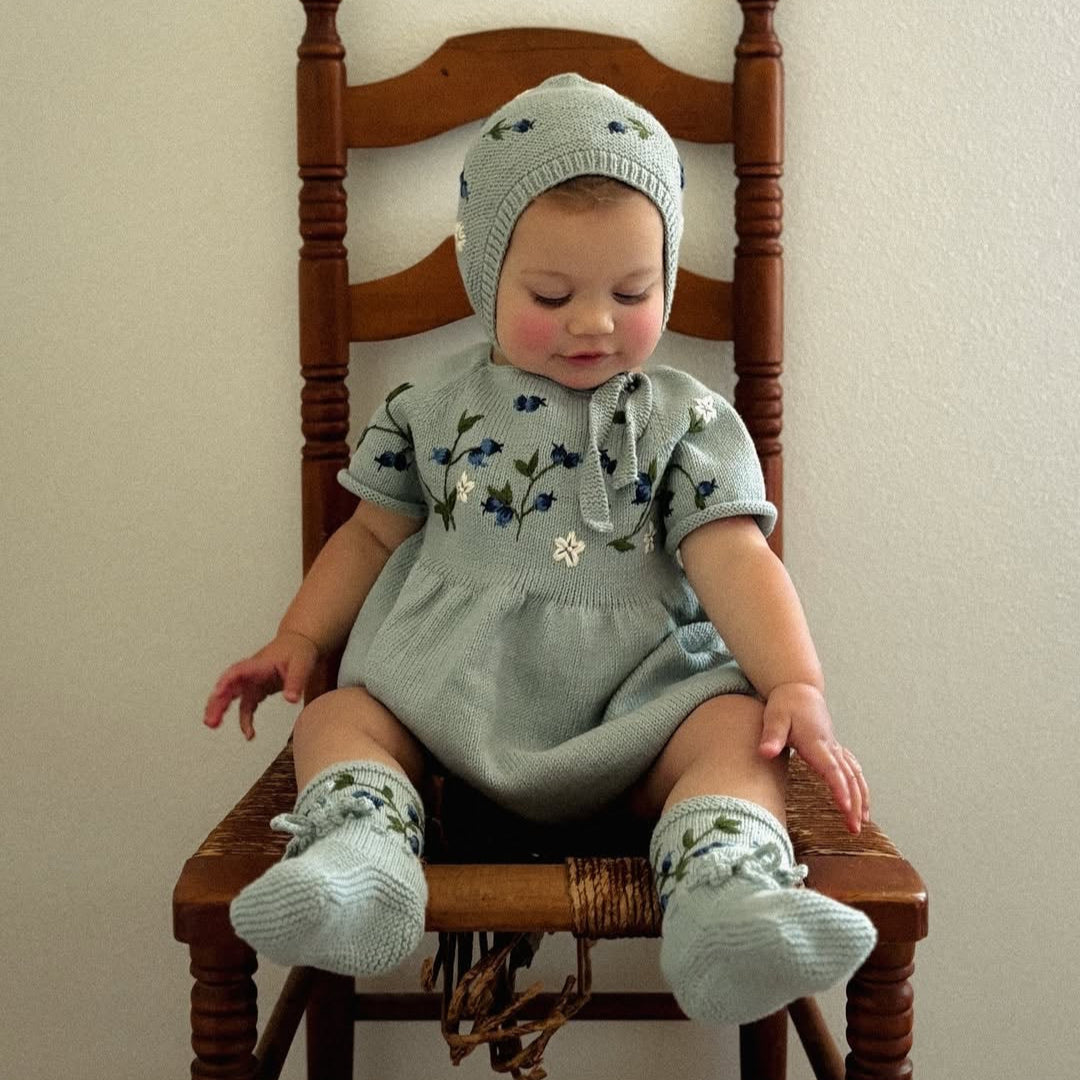 Baby sitting happily wearing matching duck blue footies and romper.