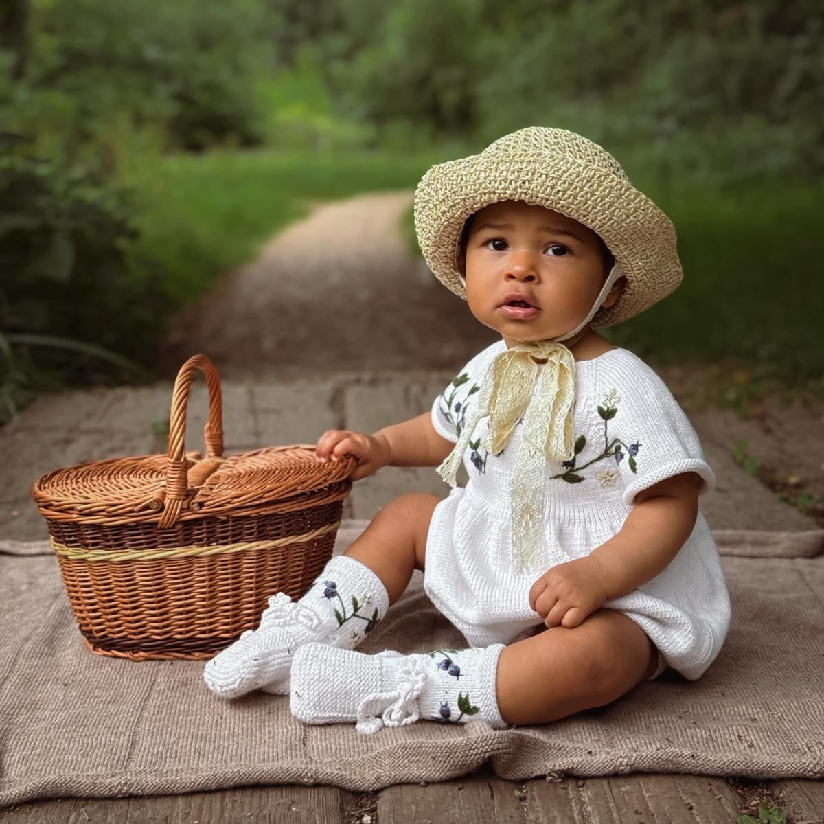 Child sitting outside wearing knitted and hand embroidered blueberries footies in Marshmallow 