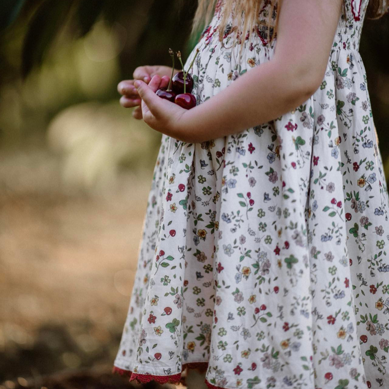 Child in a floral dress holding cherries in a natural setting